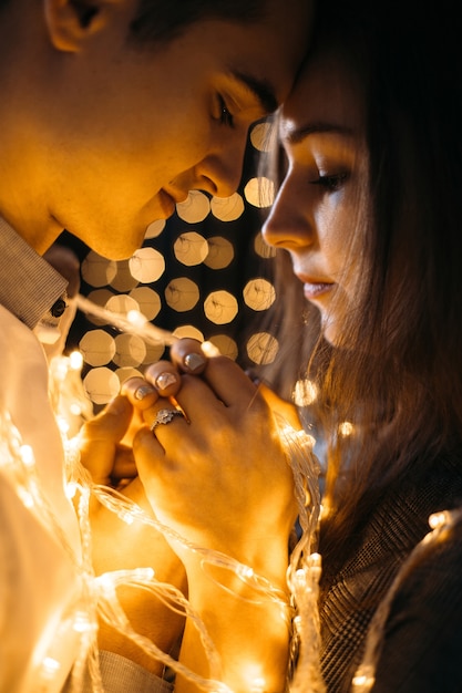 Free photo man kisses woman standing before the wall with yellow lamps