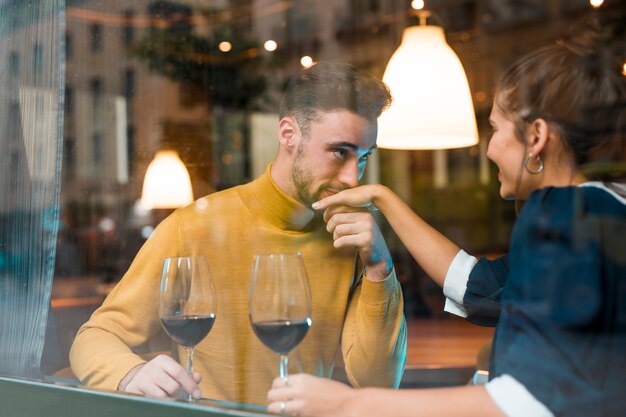 Man kissing hand of cheerful woman with glasses of wine in restaurant 