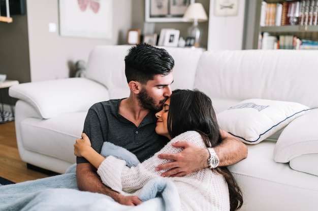 Man kissing on his girlfriend's forehead sitting in front of sofa