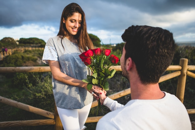 Free Photo man kneeling handing a bouquet of roses to a woman