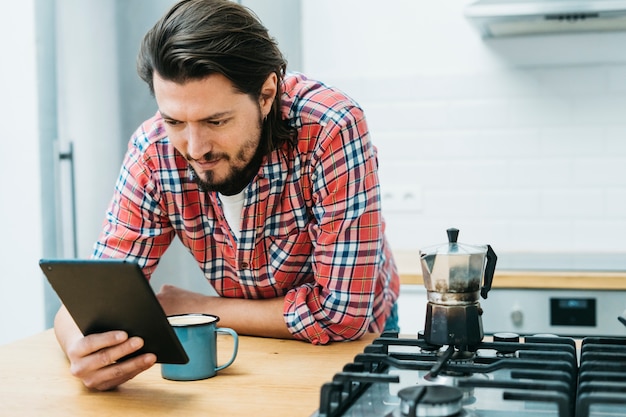 Free photo a man leaning on kitchen counter looking at smart phone