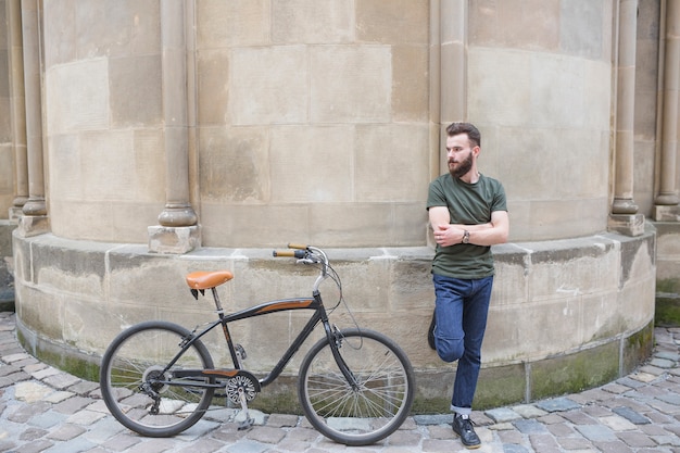 Free photo man leaning on wall next to his bicycle