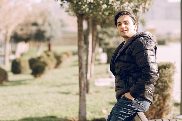 Man in leather jacket putting hands into pocket and standing in the park. High quality photo