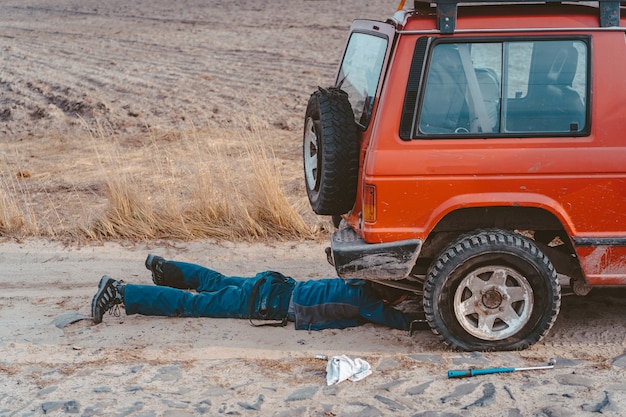 Man lies under a 4x4 car on a dirt road