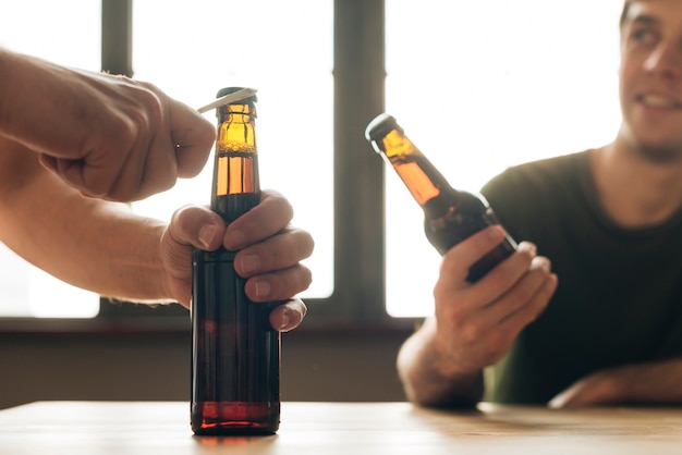 Free photo a man looking at a person opening brown beer bottle in restaurant