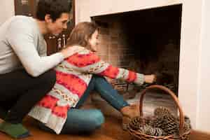 Free photo man looking at young woman placing pinecone in the fireplace