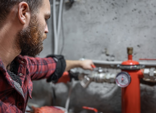 The man looks at the faucet, pipes, valve, pressure meter.