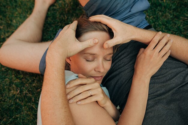 Man lying on grass and rubbing head of his wife