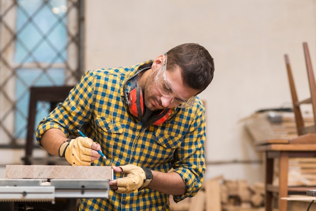 Man makes the measurements on the board with pencil in the workshop