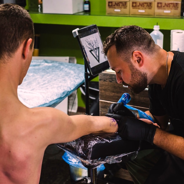 Free photo man making tattoo on arm in studio