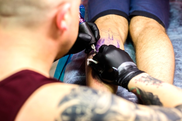 Free photo man making tattoo with needle on leg