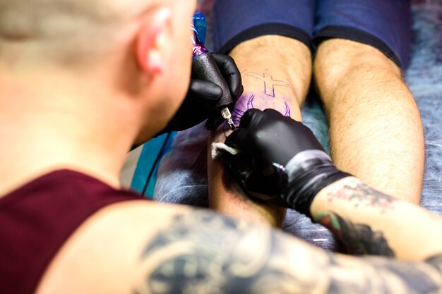 Man making tattoo with needle on leg