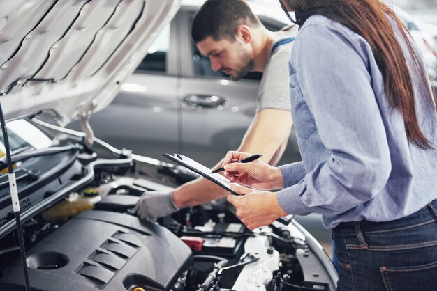 A man mechanic and woman customer look at the car hood and discuss repairs