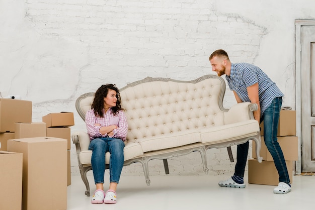 Free photo man moving sofa with sitting woman