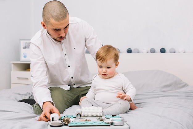 Free Photo man near little baby with toy sitting on bed