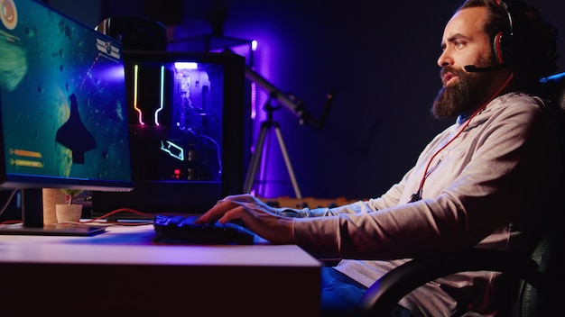 Man in neon lit apartment playing singleplayer videogame with spaceship shooting laser bullets