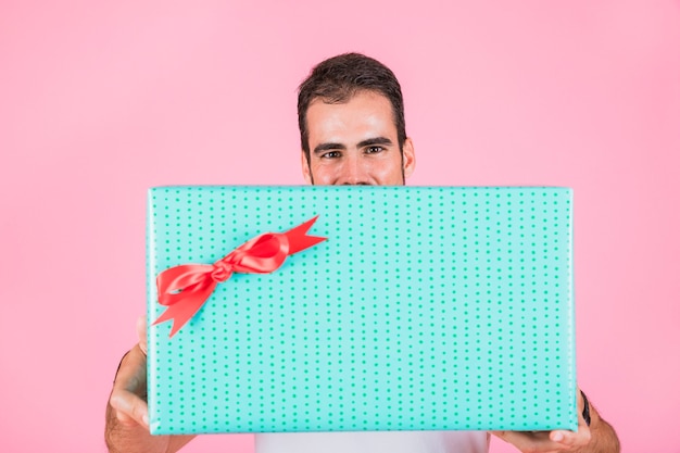 Man offering rectangular gift box standing against pink backdrop