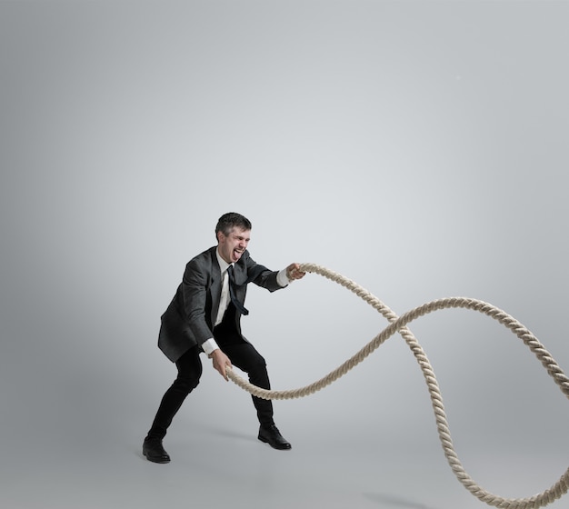 Free photo man in office clothes training with ropes on grey background.