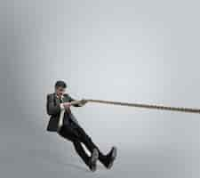 Free photo man in office clothes training with ropes on grey background.