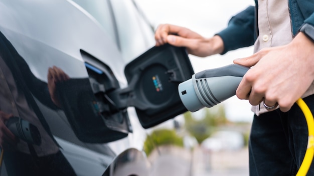 Free photo man opening cars charge socket and holding charger at charge station