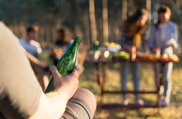 Man outdoors holding a bottle of beer with friends at the table