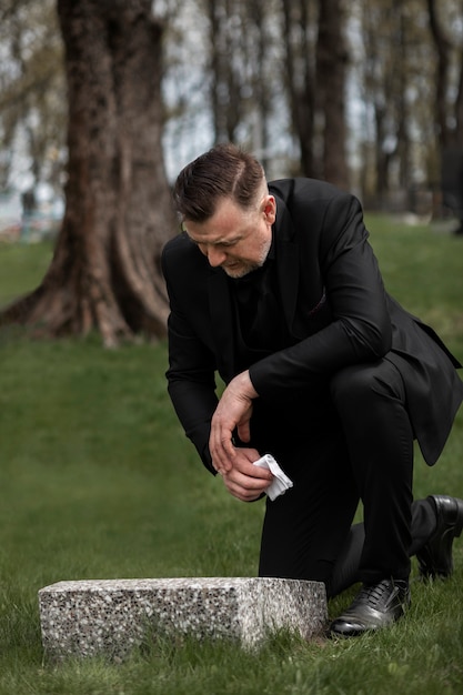 Free photo man paying respect to a tombstone at the cemetery