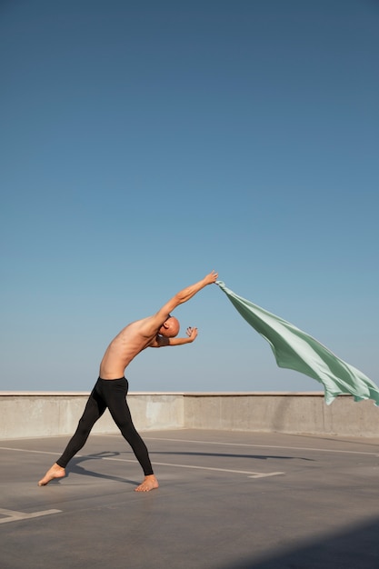 Free Photo man performing artistic dance on a rooftop with blue sky