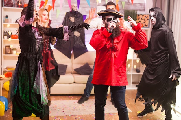 Free photo man in pirate costume doing karaoke at halloween party with his friends.