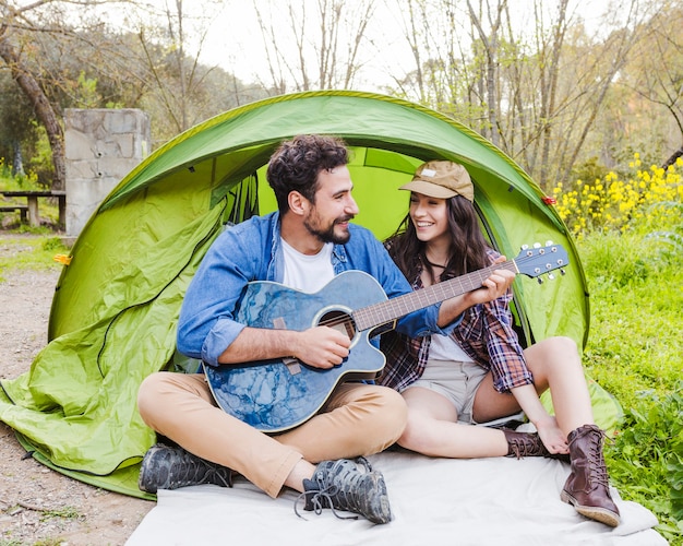 Free Photo man playing guitar for woman near tent