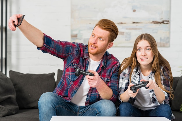 Free photo man playing video game with her girlfriend taking selfie on smartphone