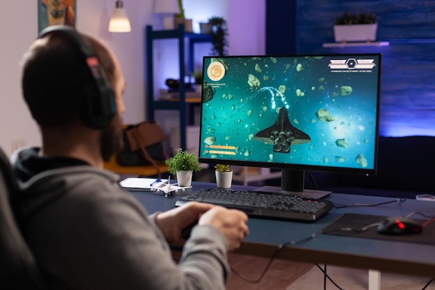 Man playing video games with controller and headphones on computer. Player using joystick and audio headset for online gaming. Gamer having fun activity with equipment to play games.