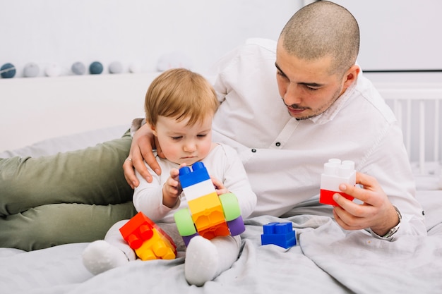 Free photo man playing with little baby holding toy building blocks