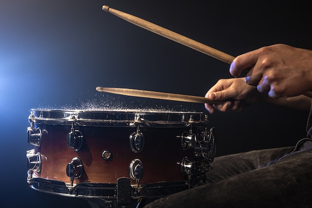 A man plays with drumsticks on a snare drum with splashing water.