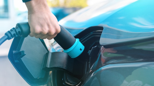 Man plugging in charger into an electric car at charge station