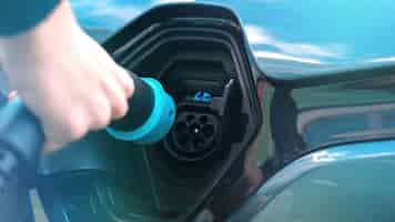 Free photo man plugging in charger into an electric car at charge station