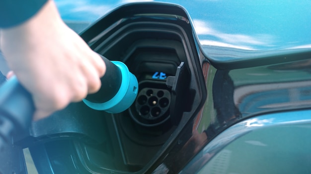 Free Photo man plugging in charger into an electric car at charge station