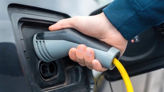 Man plugging in charger into an electric car at charge station