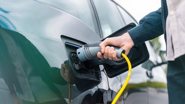 Man plugging in charger into an electric car at charge station