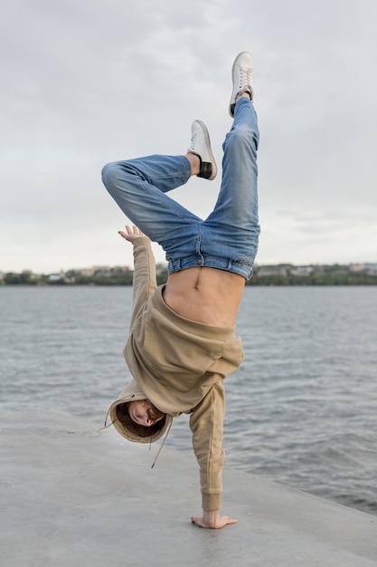 Free Photo man posing while standing in one hand next to lake