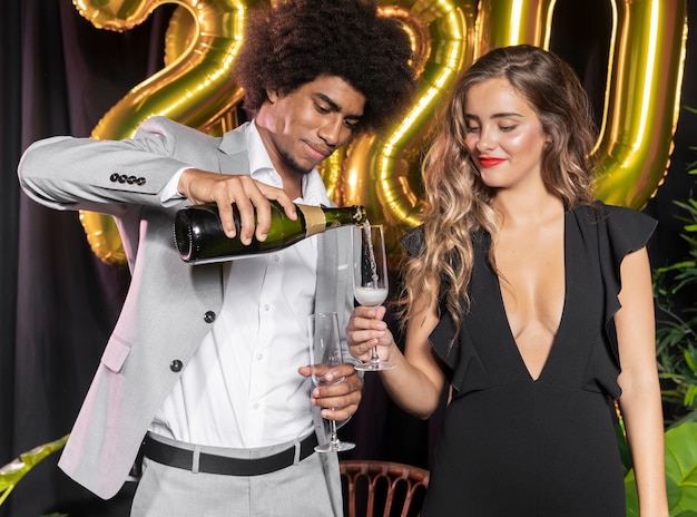 Free photo man pouring champagne in glass held by woman