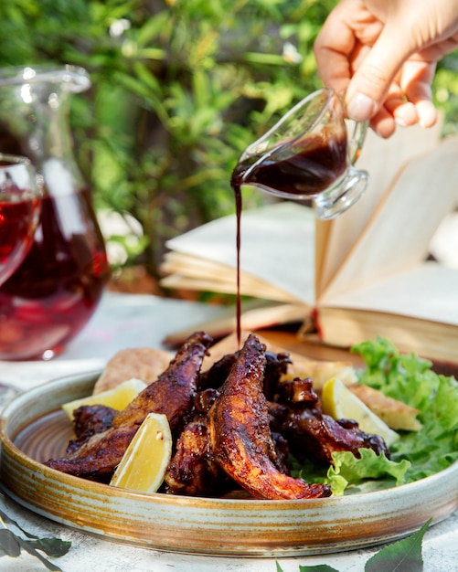 Free photo man pouring nar-sharab pomegranate sauce on the grilled chicken served with lemon