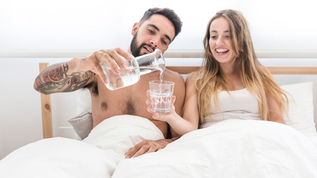 Man pouring water in glass for her wife in bedroom