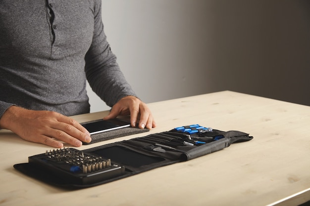 Free photo man prepares to disassemble phone at home with his personal portable tool kit on table space for your text on right side