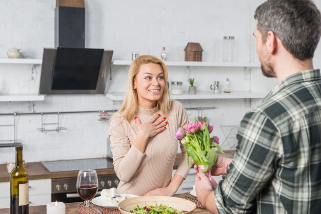 Man presenting flowers to surprised woman in kitchen 