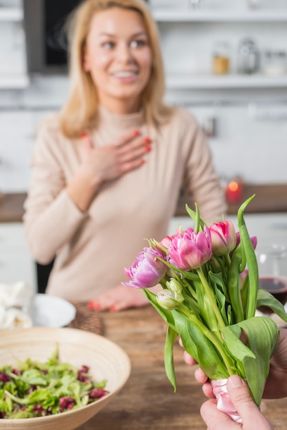 Man presenting flowers to surprised woman in kitchen