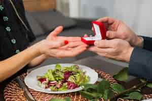 Free photo man presenting gift box with ring to woman at table with plate