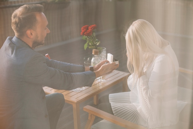 Man proposing to girlfriend offering engagement ring in restaurant