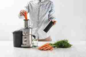 Free photo man puts carrots inside metallic juicer with empty glass to make tasty juice for breakfast