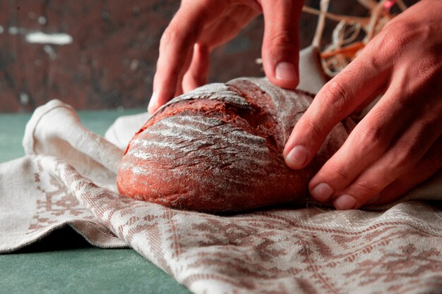 Man putting homemade wheat bread with flour on it on a white towel with two hands.