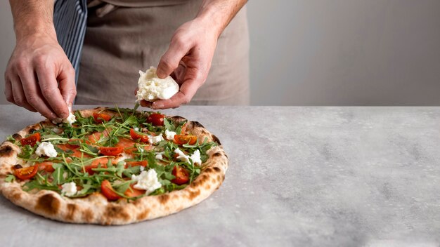 Man putting mozzarella on baked pizza dough with smoked salmon slices